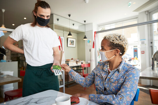 Mid adult woman making contactless payment in cafe during COVID-19