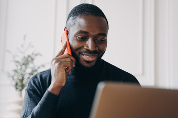 Cheerful young man with African lineage commerce businessowner calling to supplier for confirmation