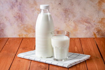 Bottle and glass of milk on a brown wooden table background. Rustic food still life. Cooking ingredient, drink. A source of calcium.