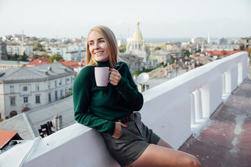 beautiful blonde woman on the roof of the attic looks at the city