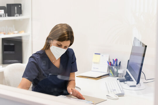 Female dentist wearing protective face mask working at desk in clinic