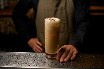 great view on glass with whipped creamy cocktail on bar and male barman hand holds it