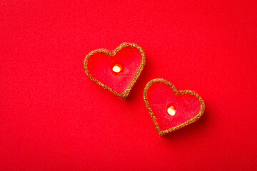 Top-down view of two candles in shape of hearts on bright red background. Love concept