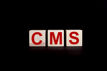 acronym CMS Content Management System. Three wooden cubes, blocks lie on a black background. Business idea.