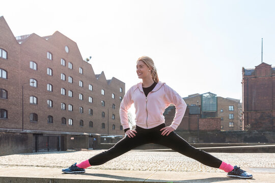 Smiling flexible young woman looking away while practicing splits in city