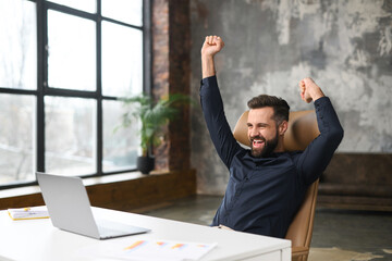 Excited young businessman in smart casual wear celebrating successful deal, looking at monitor...
