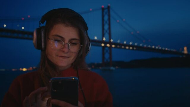 Pretty young woman in big headphones listen to music and use smartphone to scroll through application and social media feed, choose music or podcast to listen to on streaming platform