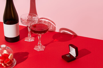 Marriage proposal valentines day concept. Ring, sparkling wine, glasses and candies on red table