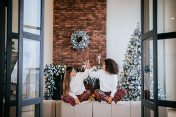 Two female student friends sitting on the couch at home. High five