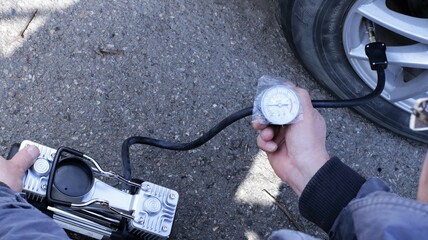 inflating a deflated wheel with an electric pump and monitoring the air pressure in the tires, checking and inflating a tire on the road, a man pumps the wheels of a car using a portable pump