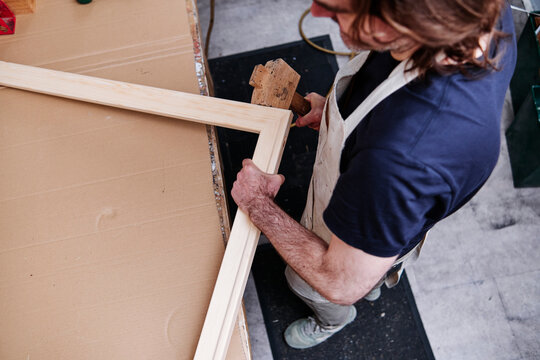 Craftsman using hammer while making wooden frame in workshop
