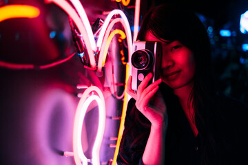 Young female photographer photographing neon lighting with retro style camera