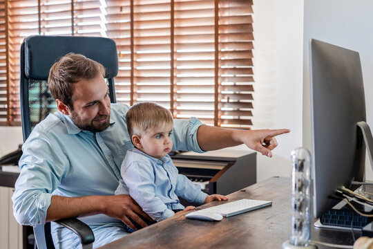 Smiling father pointing at computer while son sitting on lap at home
