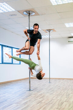 Male acrobat supporting woman while holding hands during rehearsal on rod in dance studio
