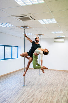 Male acrobat carrying female dancer while hanging on rod in dance studio