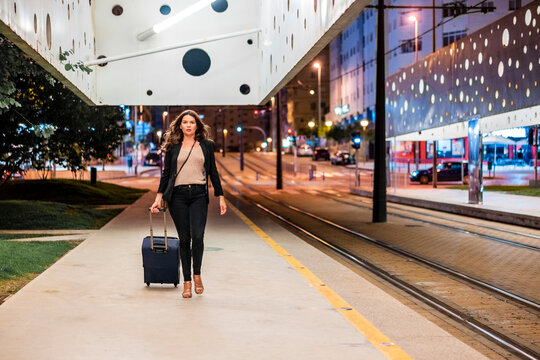 Businesswoman pulling wheeled luggage while walking on platform at night
