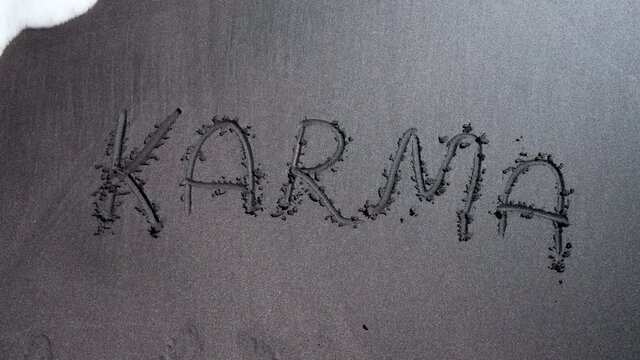 Word karma written on black sand beach, washed away by sea or ocean wave. Cause and effect. Concept of religion, esotericism, buddhism, world harmony and universe balance.