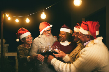 Diverse senior people having fun cheering with wine during Christmas eve wearing Santa Clause hats...