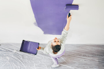 Funny woman painting wall. Woman with paint roller painting wall. Repair and house renovation...