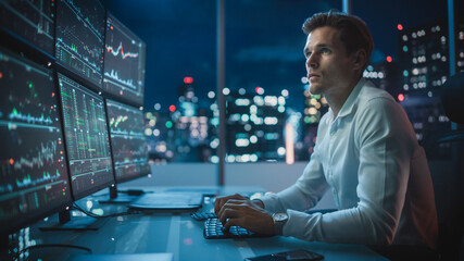 Fototapeta premium Financial Analyst Working on a Computer with Multi-Monitor Workstation with Real-Time Stocks, Commodities and Exchange Market Charts. Businessman Works in Investment Bank Downtown Office at Night.