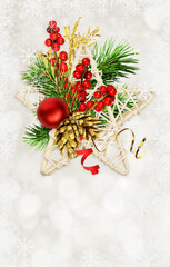 Christmas arrangement with green pine twigs, red berries and rattan star on white bokeh background with snowflakes