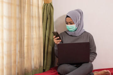 Asian women wearing hijabs wearing masks are working from home