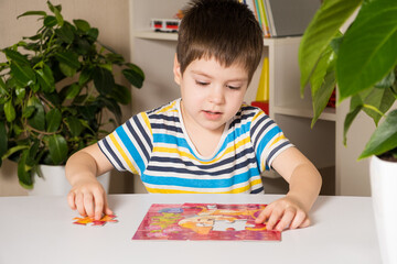 A boy in a striped T-shirt plays puzzles, collects a picture of a cat.