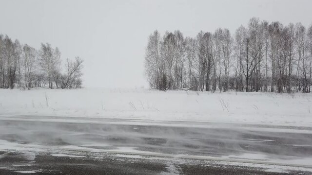 Steadicam shot of siberian intercity highway when car drove past camera from right to left. Strong wind and heavy snowstorm in evening. Snowed fields and some trees are behind the road