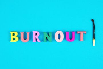 Word burnout from multicolored wooden letters and burnt match on blue background. Burnout metaphor. State of emotional, physical, and mental exhaustion caused by excessive and prolonged stress