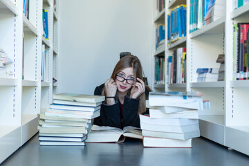 Young female student, among a stack of books on the floor, studying in a library