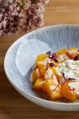 baked pumpkin in ceramic plate close up wooden table with glass of white wine. pumpkin with stracciatella and microgreen