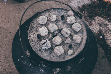dutch oven covered with light gray coals for cooking in it