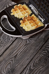 Waffle maker with waffles. On black pine boards. Close-up shot.