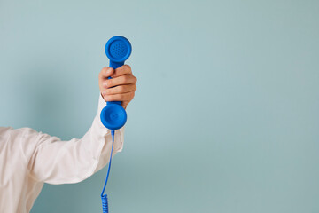 Hand of unknown man holds blue wired retro phone which is symbol of emergency call. Retro telephone handset on light blue background with empty space for text on right. Helpline concept. Banner. - obrazy, fototapety, plakaty