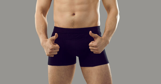 Young macho man who takes viagra is showing thumbs up standing isolated on grey background. Handsome male in boxer briefs with good sexual health and fit attractive body advertises impotence treatment