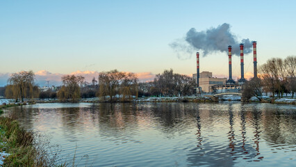 Smoking chimneys of thermal power plants near the waterfront in city. Winter. Industrial and nature background.