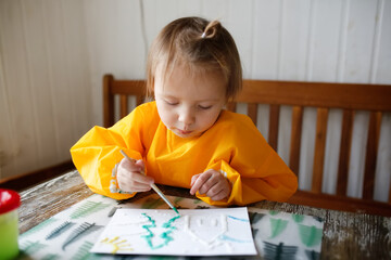 cute caucasian child Toddler is engaged in creativity in a yellow protective apron, the child draws with paints on salt, unusual drawing and developmental activities