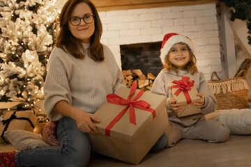 Obraz na płótnie Canvas Christmas spirit. Happy mother and dauther with christmas gift box sitting on the floor near the Christmas tree. Happy family with christmas present box. Holidays and celebrations concept