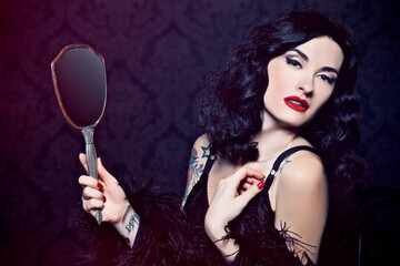 Retro burlesque diva with tattoes holding a mirror