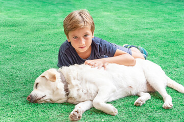 Blond boy hugging his dog lying on the grass. Concept of love for animals