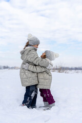 Funny girls hugging in the winter in the snow. Happy sisters play snow games. Children Friends are happy to be together on a cold winter day