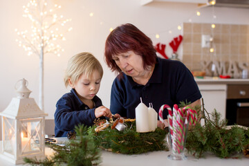 Cute toddler blond child, boy, decorating christmas advent wreath at home with his grandmother