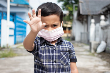 Asian little boy wears a mask to protect and shows stop hand