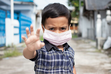 Asian little boy wears a mask to protect and shows stop hand