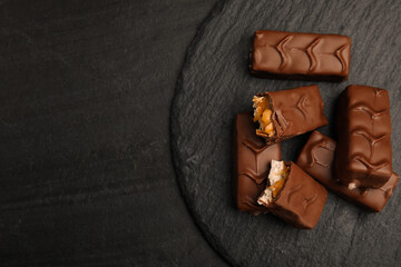 Slate plate of chocolate bars with caramel, nuts and nougat on black table, top view. Space for text