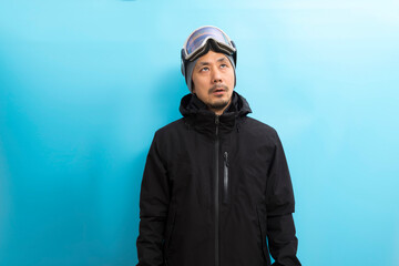 Winter sport. Handsome asian man with snowboard goggles and black anorak coat with curious face...