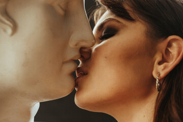Obraz premium Beautiful young woman kissing a plaster statue of David's head. Girl flirts with a sculpture of a bust of Apollo. Relationship with a man. Beautiful woman with bright makeup