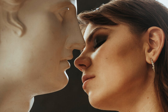Beautiful young woman kissing a plaster statue of David's head. Girl flirts with a sculpture of a bust of Apollo. Relationship with a man. Beautiful woman with bright makeup