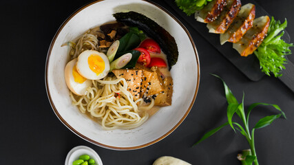 Asian dinner, bowl of vegetarian ramen with tofu, gyoza and nikuman bun a black background,...