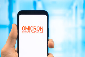 Doctor hand holds mobile phone with text Omicron variant of coronavirus. Hospital background....